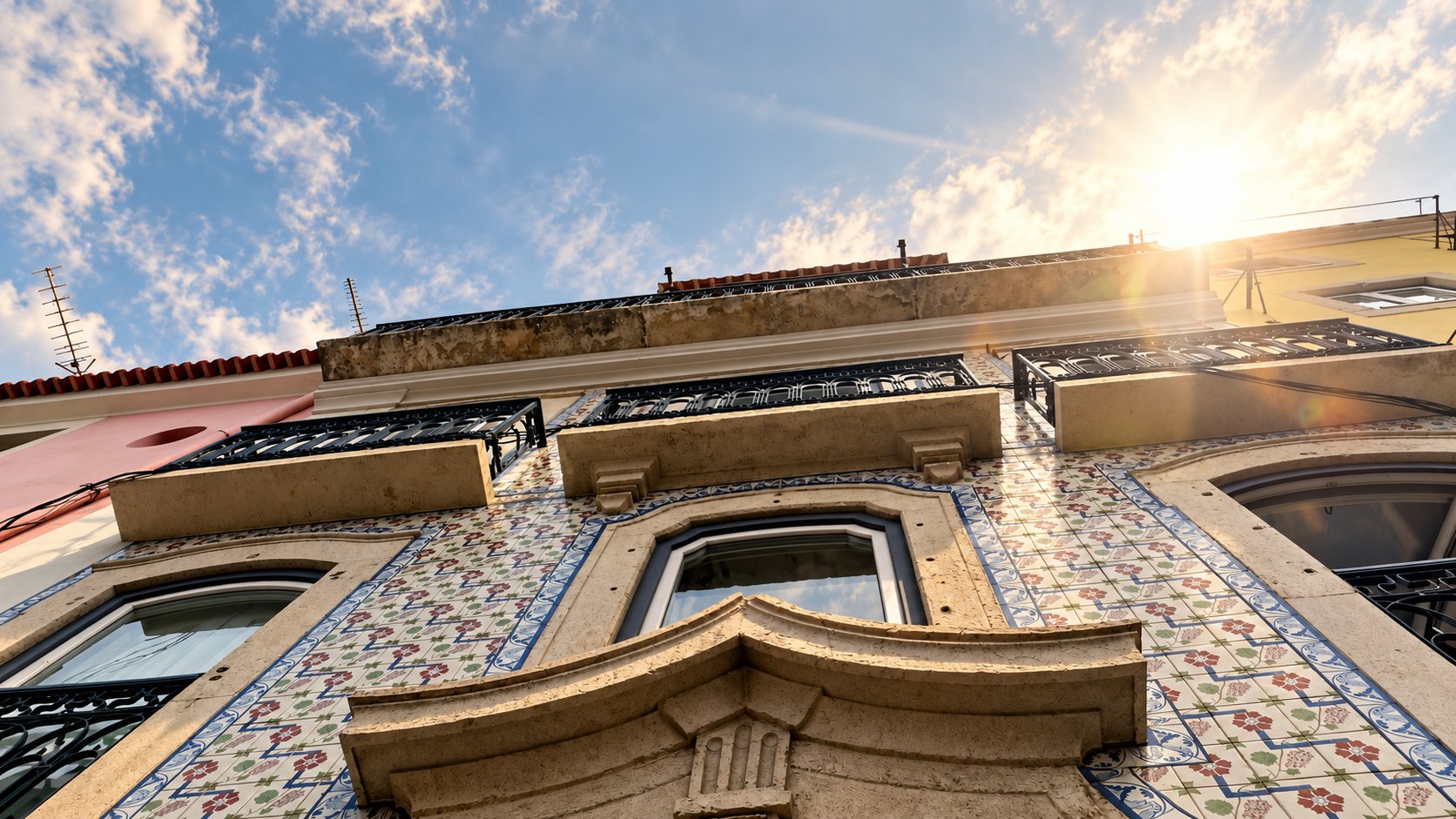 Fachada azulejada da sede da PT.EL, vista de baixo, com o sol a nascer sobre o beiral